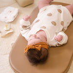 Baby lying on a wipeable change pad with a white blanket and pink socks in the background