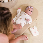 Baby lying on a wipeable change pad with a woman sitting nearby, surrounded by toys.