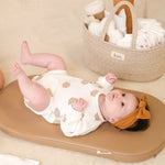 Baby lying on a wipeable change pad with a basket of baby items in the background