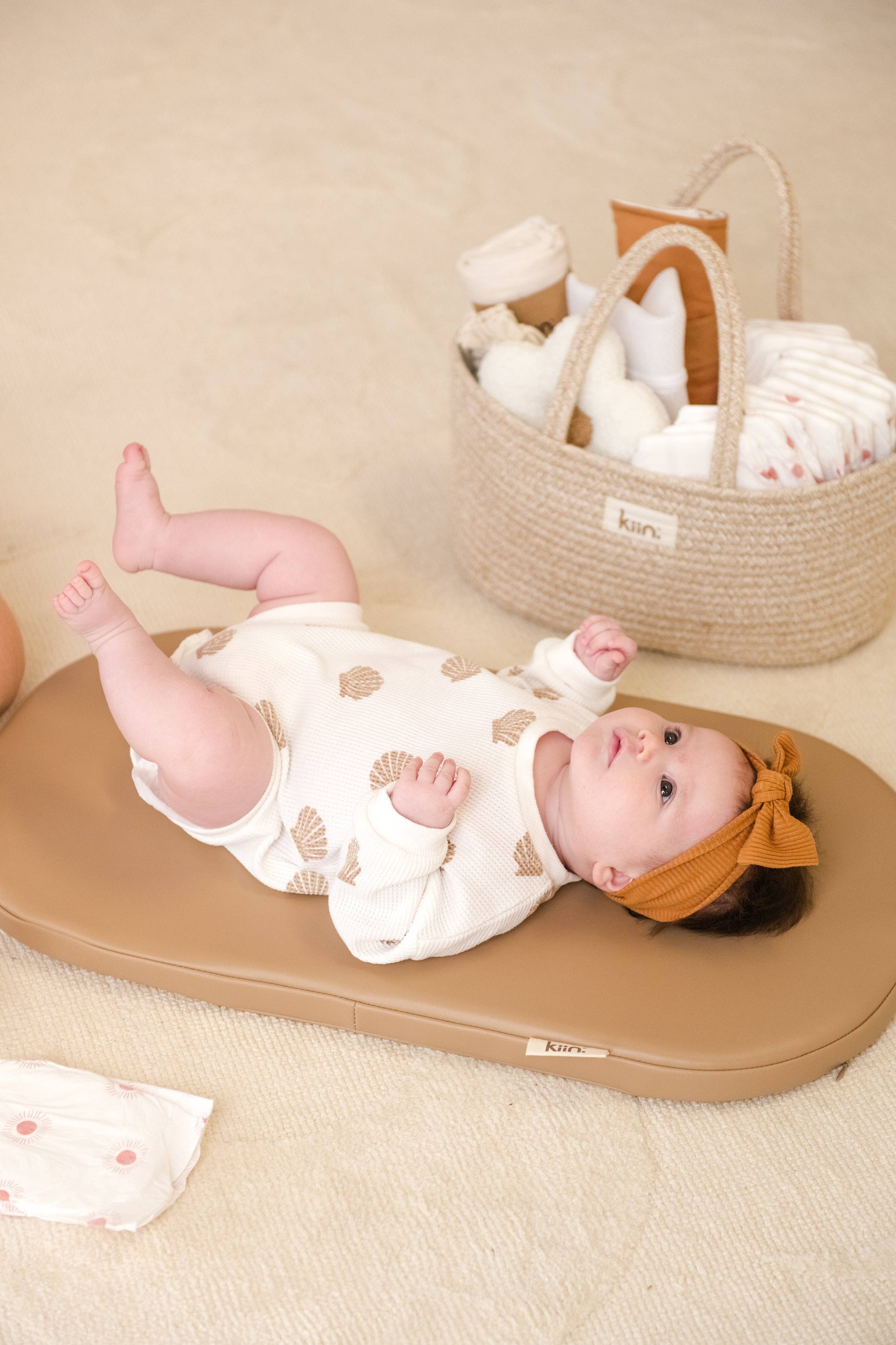 Baby lying on a wipeable change pad with a basket of baby items in the background