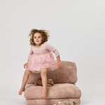 Child in a pink dress sitting on a plush chair with a white background