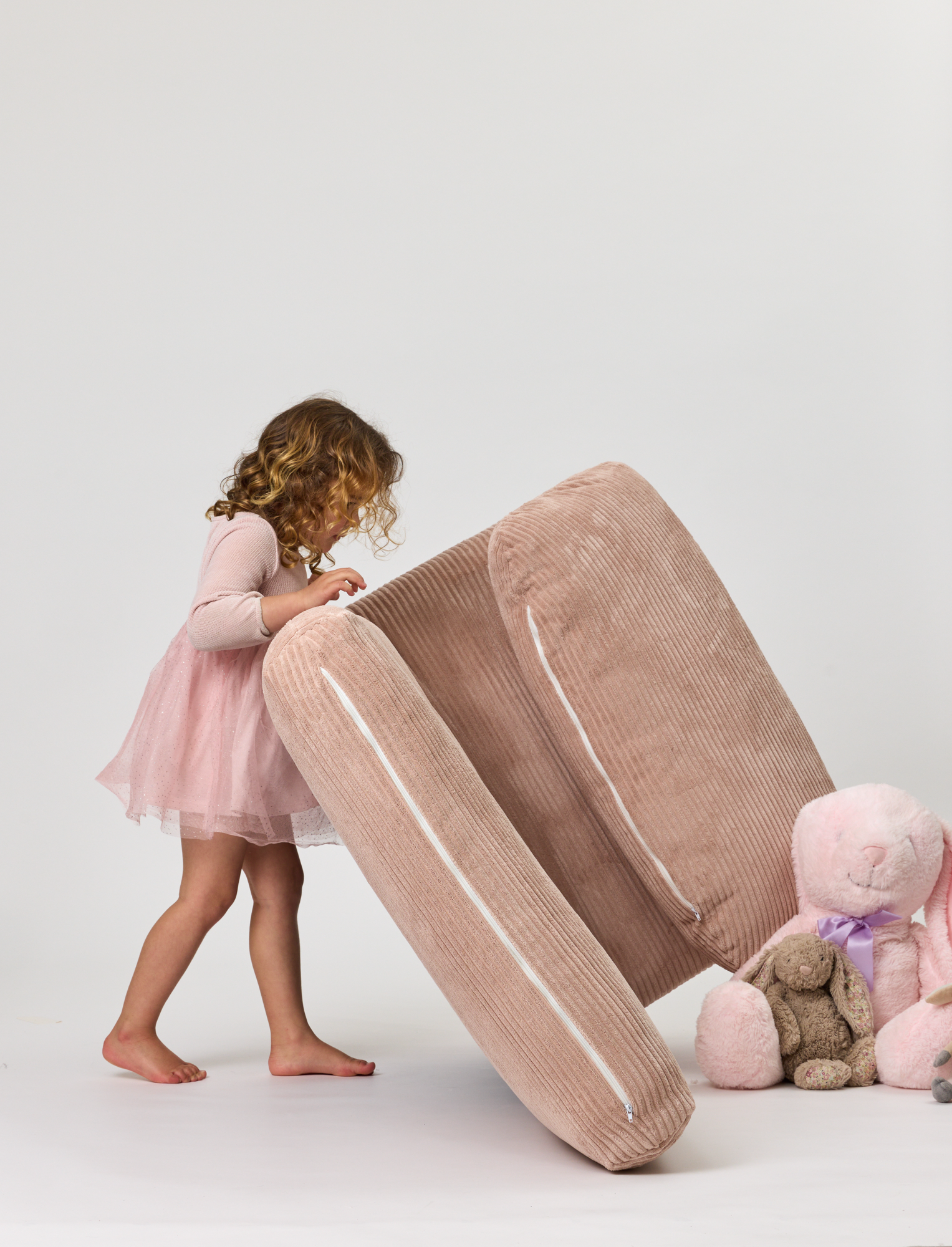 Child in a pink dress interacting with a Rylee Recliner on a white background