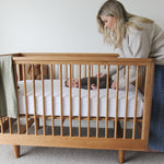 Mother tending to a baby in a George wooden cot with a light green blanket.