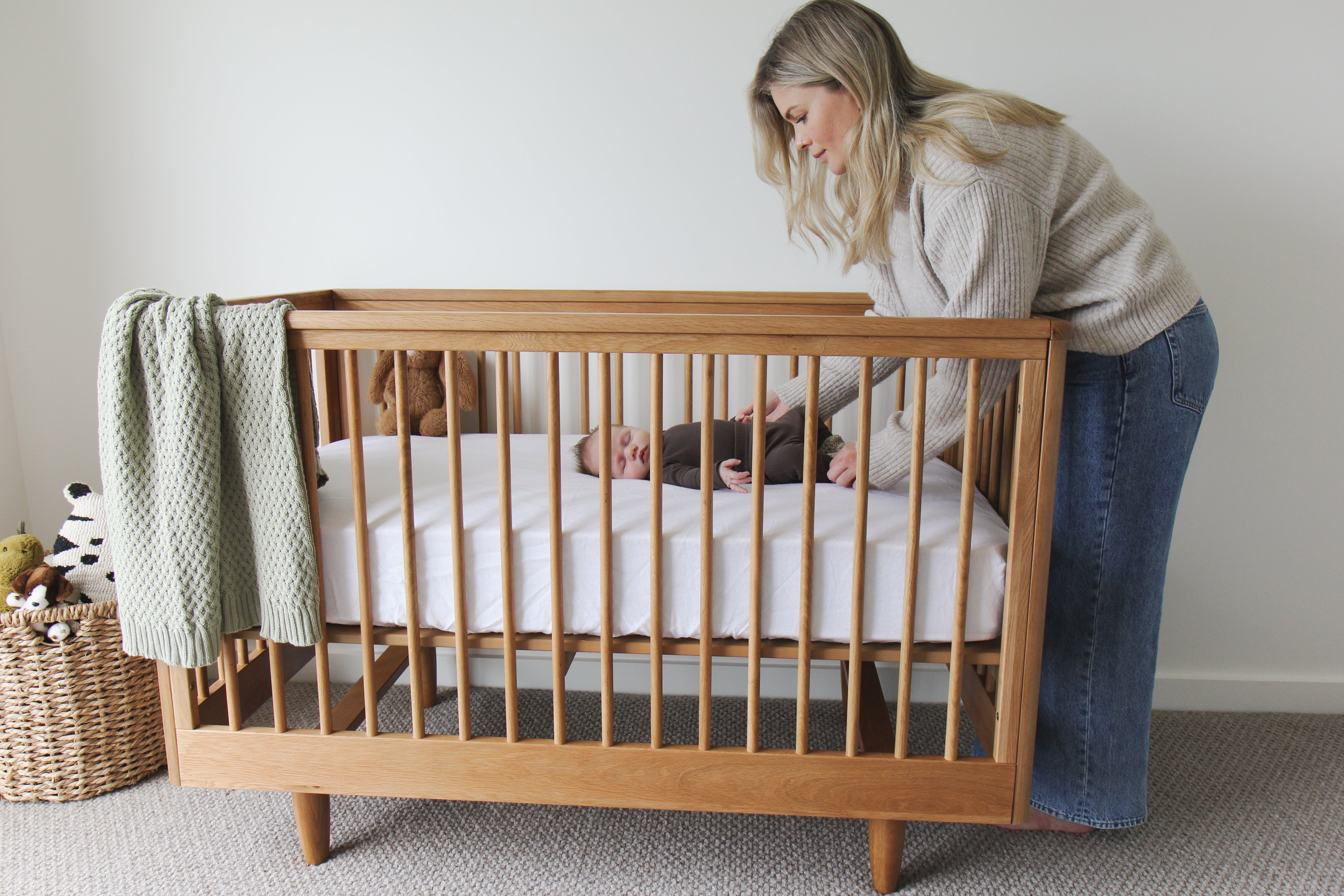 Mother tending to a baby in a George wooden cot with a light green blanket.
