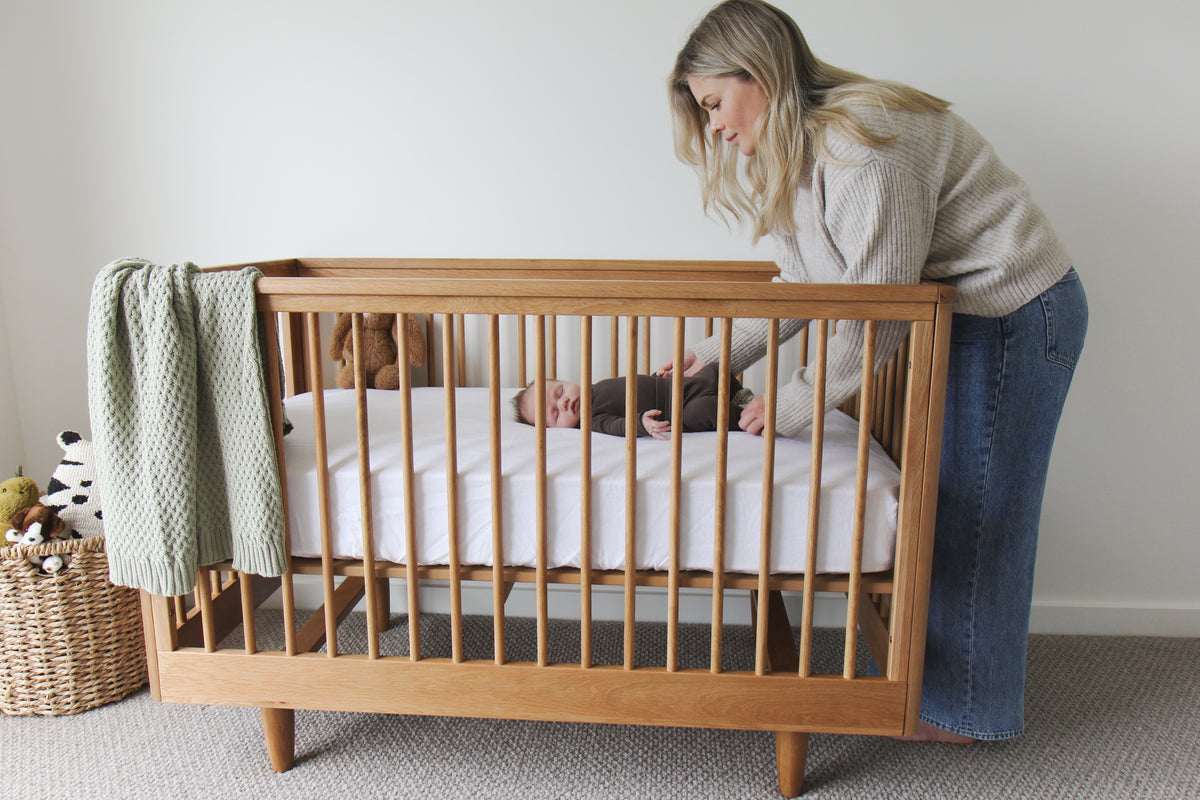 Mother tending to a baby in a George wooden cot with a light green blanket.