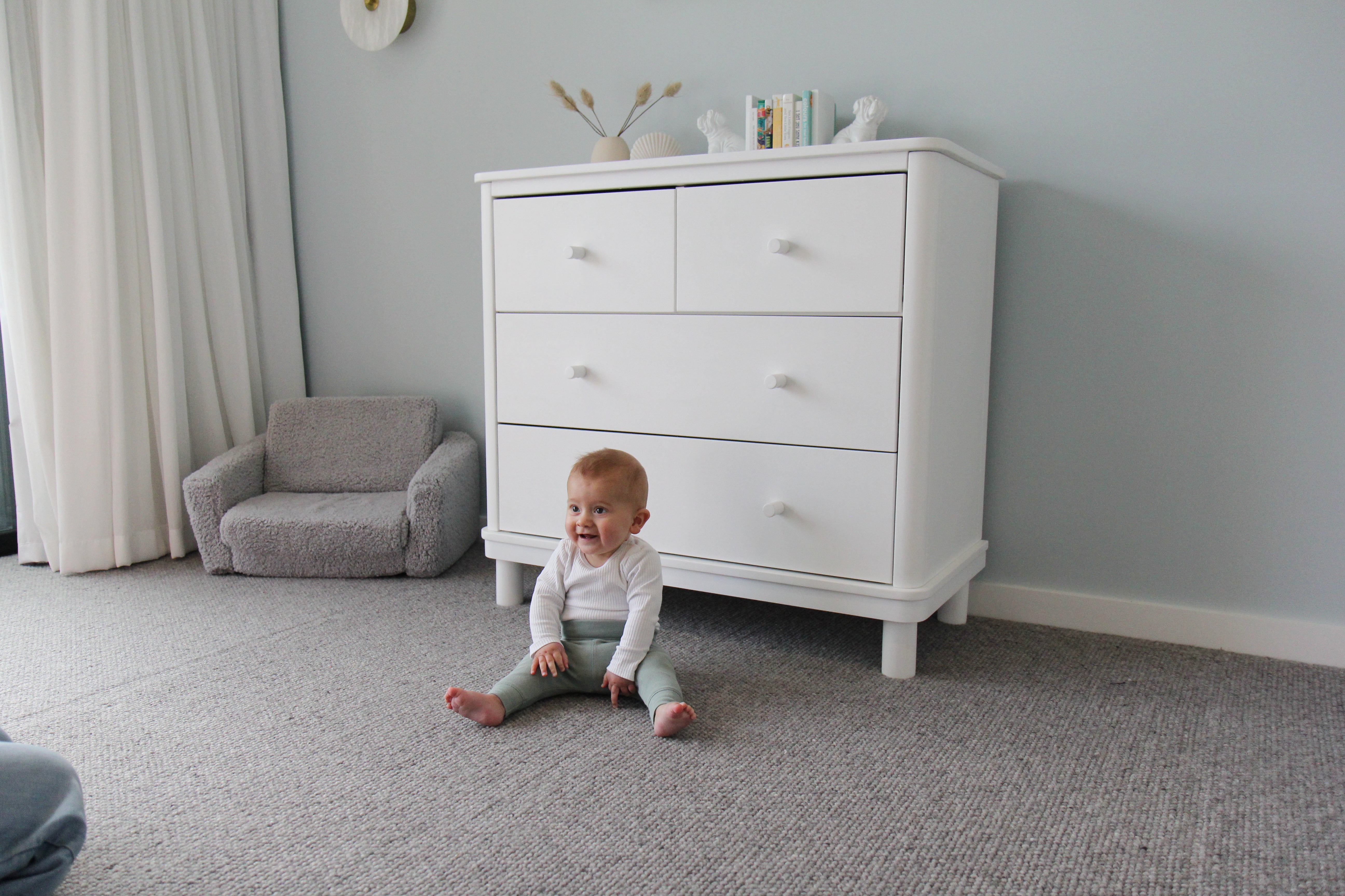 Baby sitting on the floor in front of a Florence dresser in a room with gray walls and carpet.