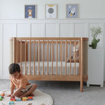 Child playing with toys on the floor next to an Indi Cot  in a nursery.