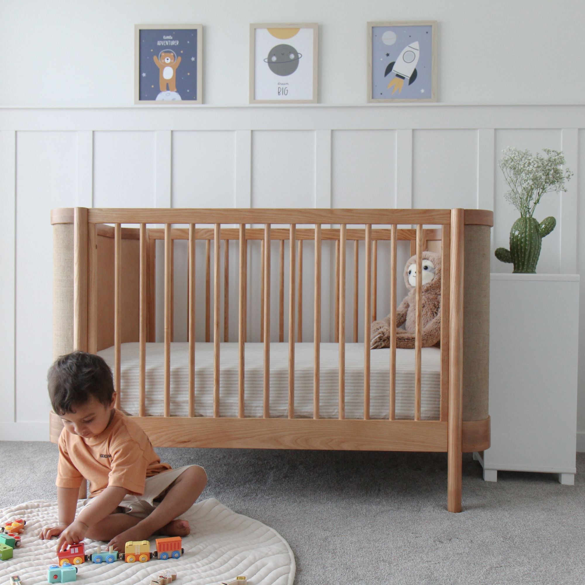 Child playing with toys on the floor next to an Indi Cot  in a nursery.