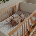Baby lying in a cot with a wooden frame and patterned mattress cover.