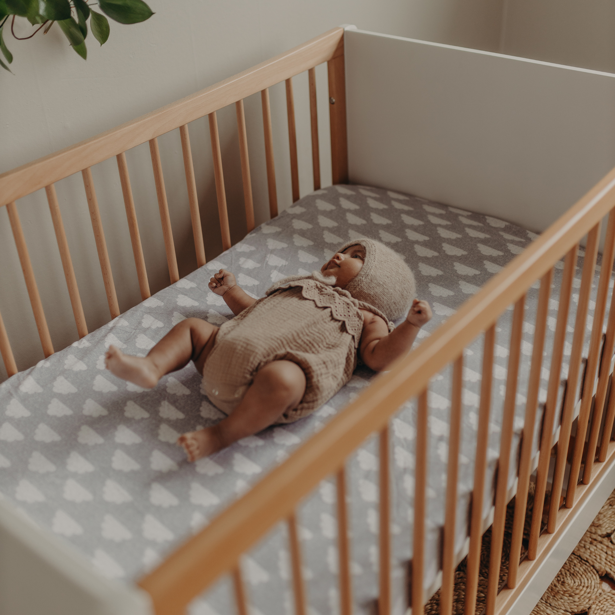 Baby lying in a cot with a wooden frame and patterned mattress cover.