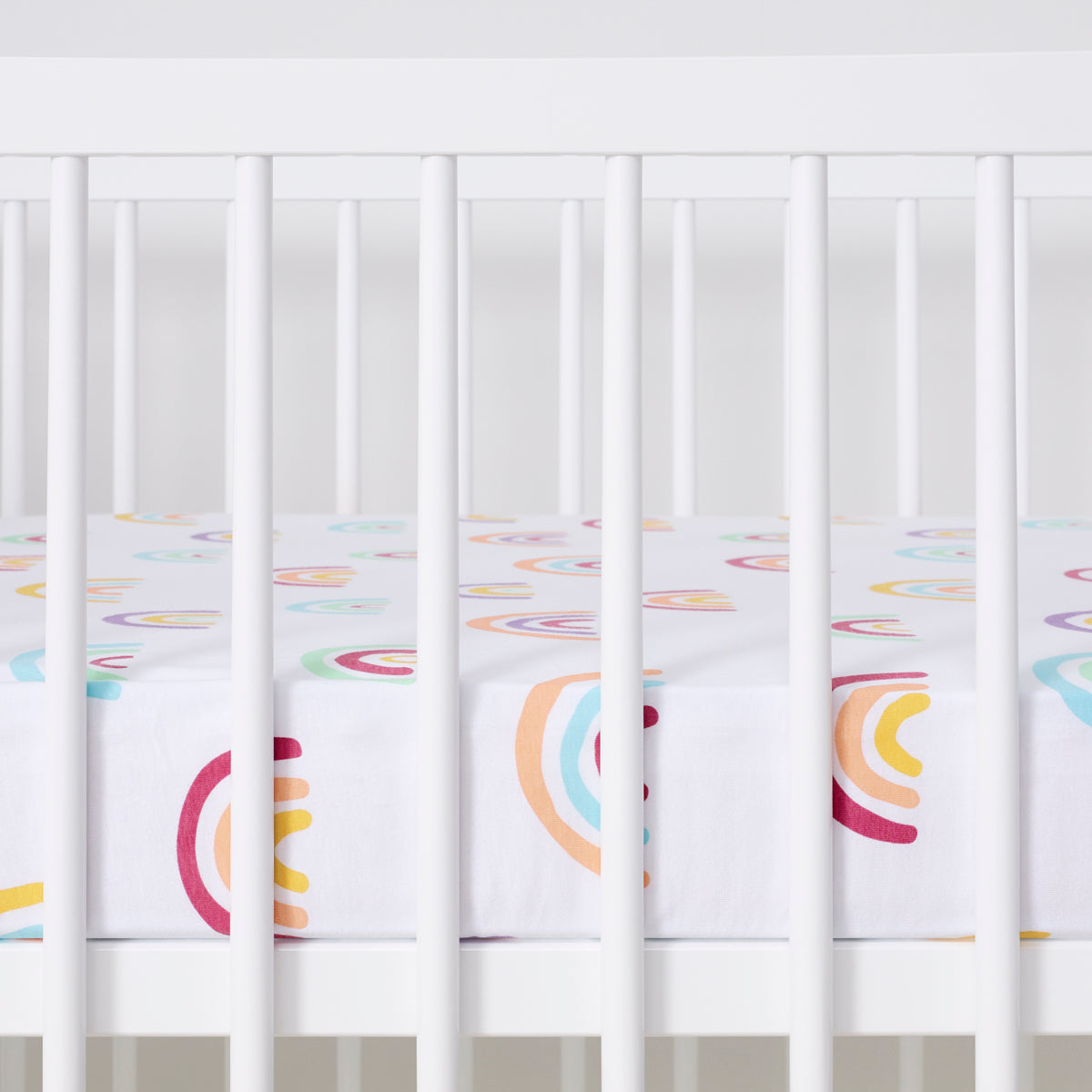 Crib with colorful rainbow patterned sheet on a white background