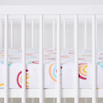 Crib with colorful rainbow patterned sheet on a white background