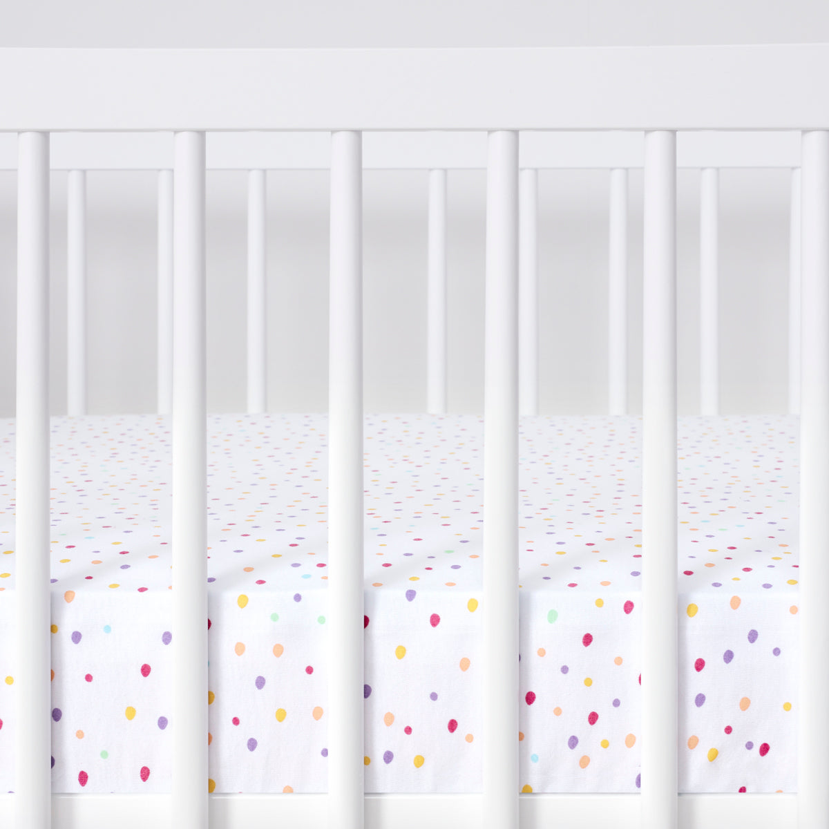 Cot with colorful polka dot crib sheet on a white background