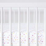 Cot with colorful polka dot crib sheet on a white background