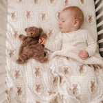 Baby sleeping with a teddy bear on a crib sheet with teddy bear pattern
