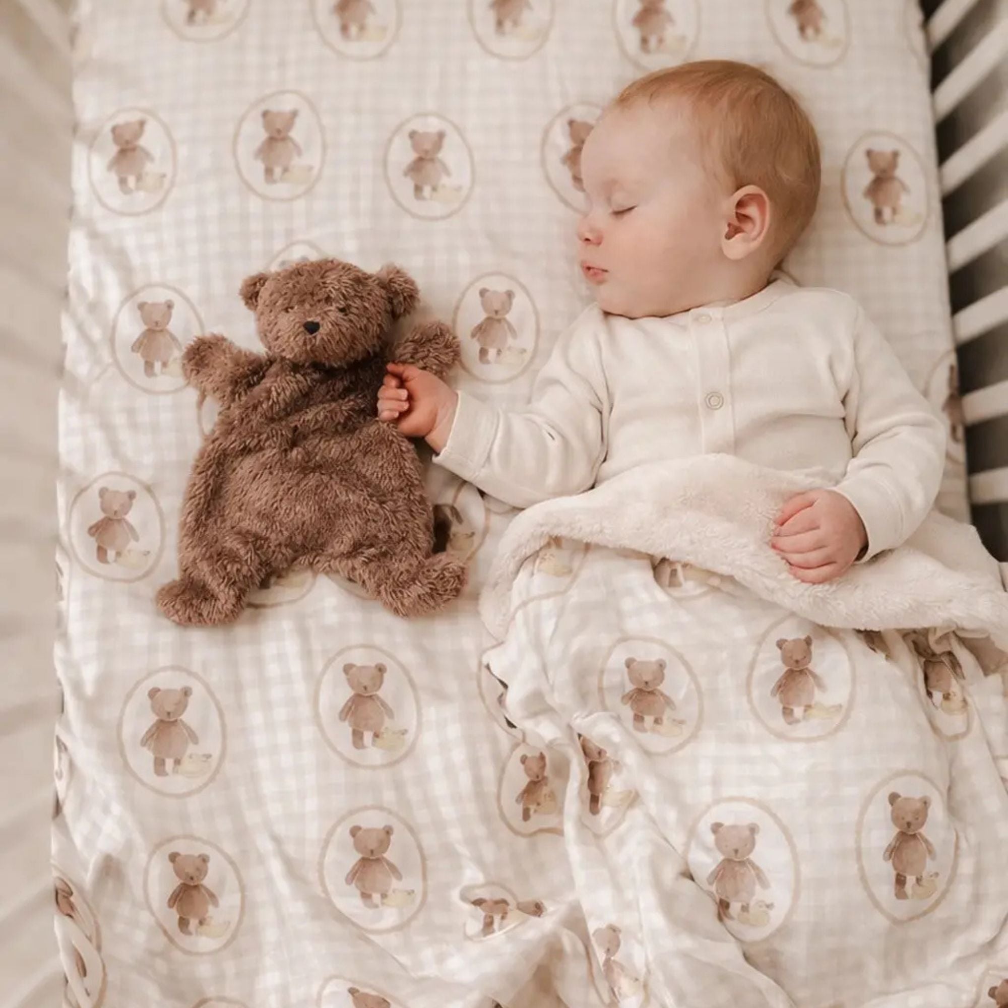 Baby sleeping with a teddy bear on a crib sheet with teddy bear pattern