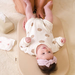 Baby lying on a wipeable change pad with a mother holding their feet, on a light-colored carpet.