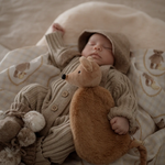 Baby in a knitted outfit holding a Squeaky the Sweet Comforter Toy, surrounded by soft bedding.