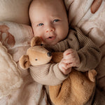 Baby holding a squeaky the sweet comforter toy surrounded by soft textures and colors
