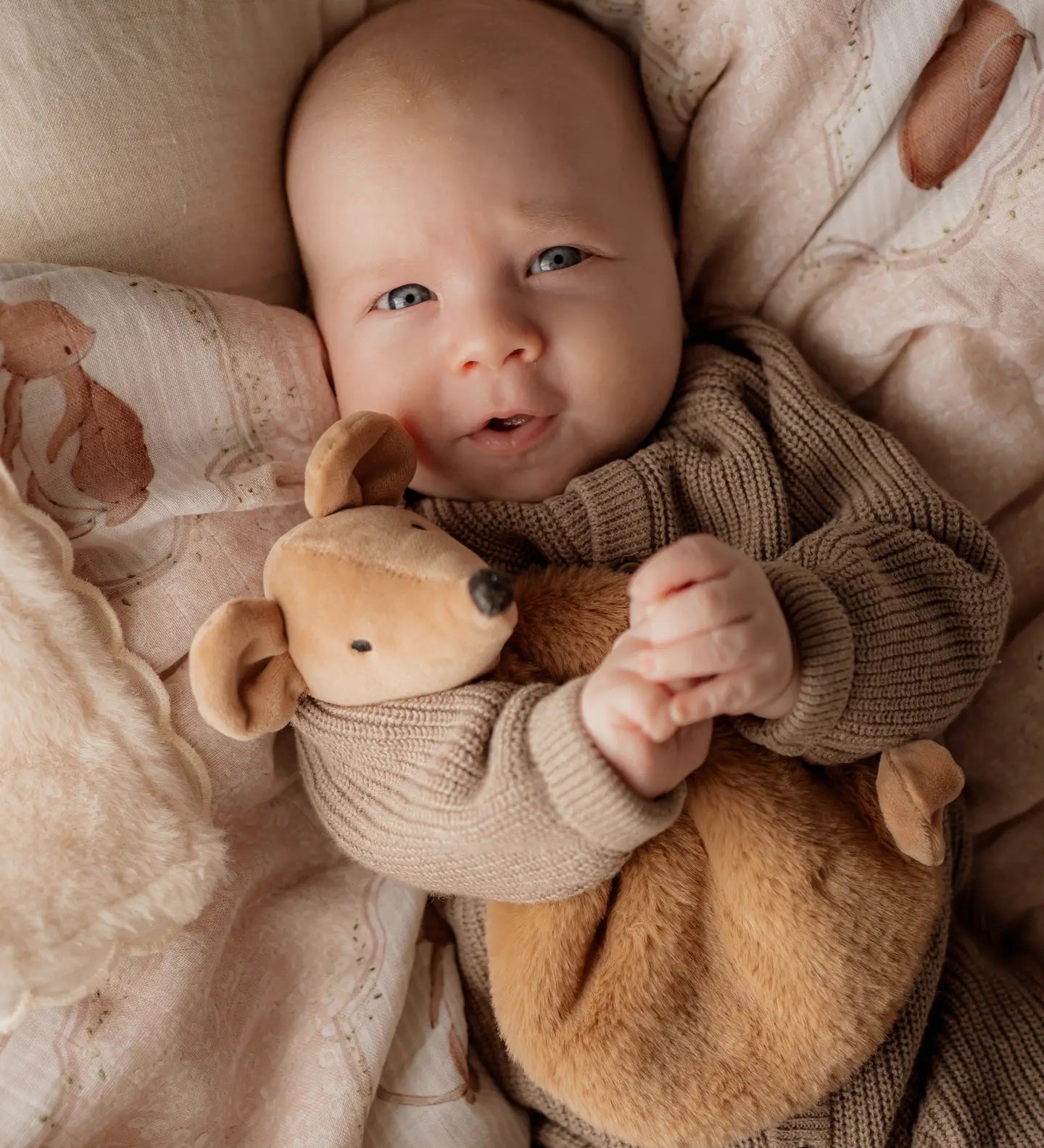 Baby holding a squeaky the sweet comforter toy surrounded by soft textures and colors