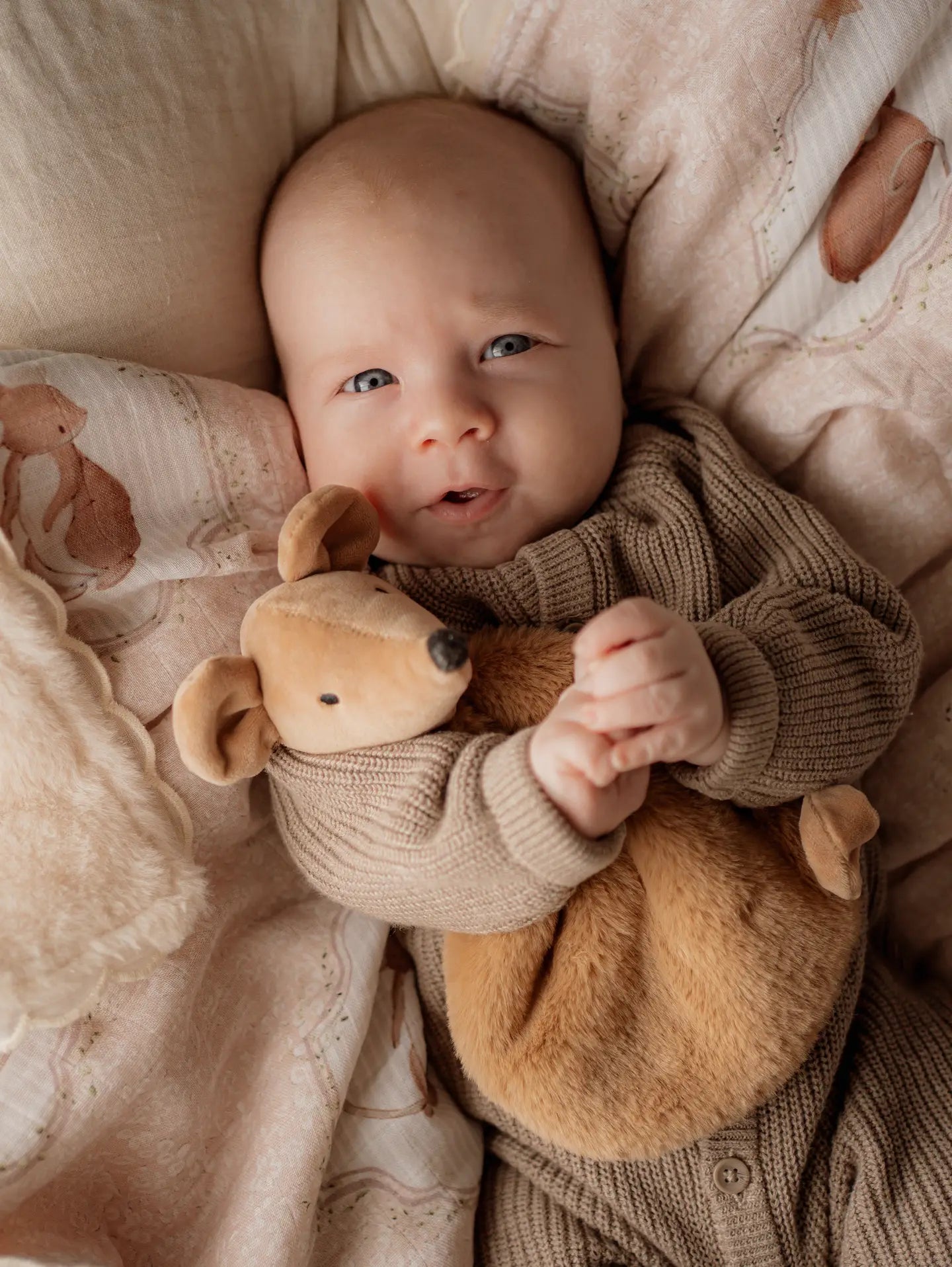 Baby holding a squeaky the sweet comforter toy surrounded by soft textures and colors