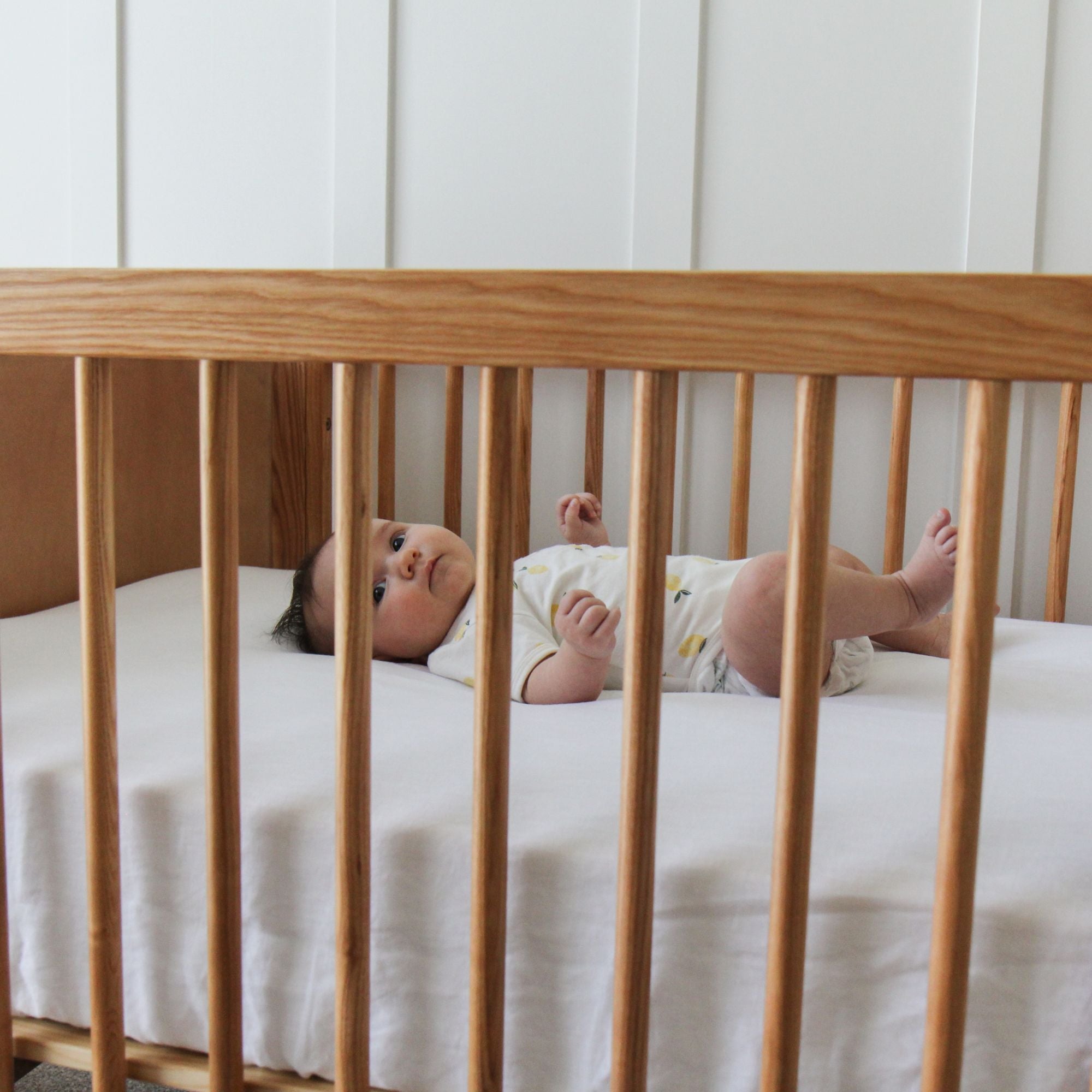 Baby lying in an Indi Cot from Cariboo with white bedding